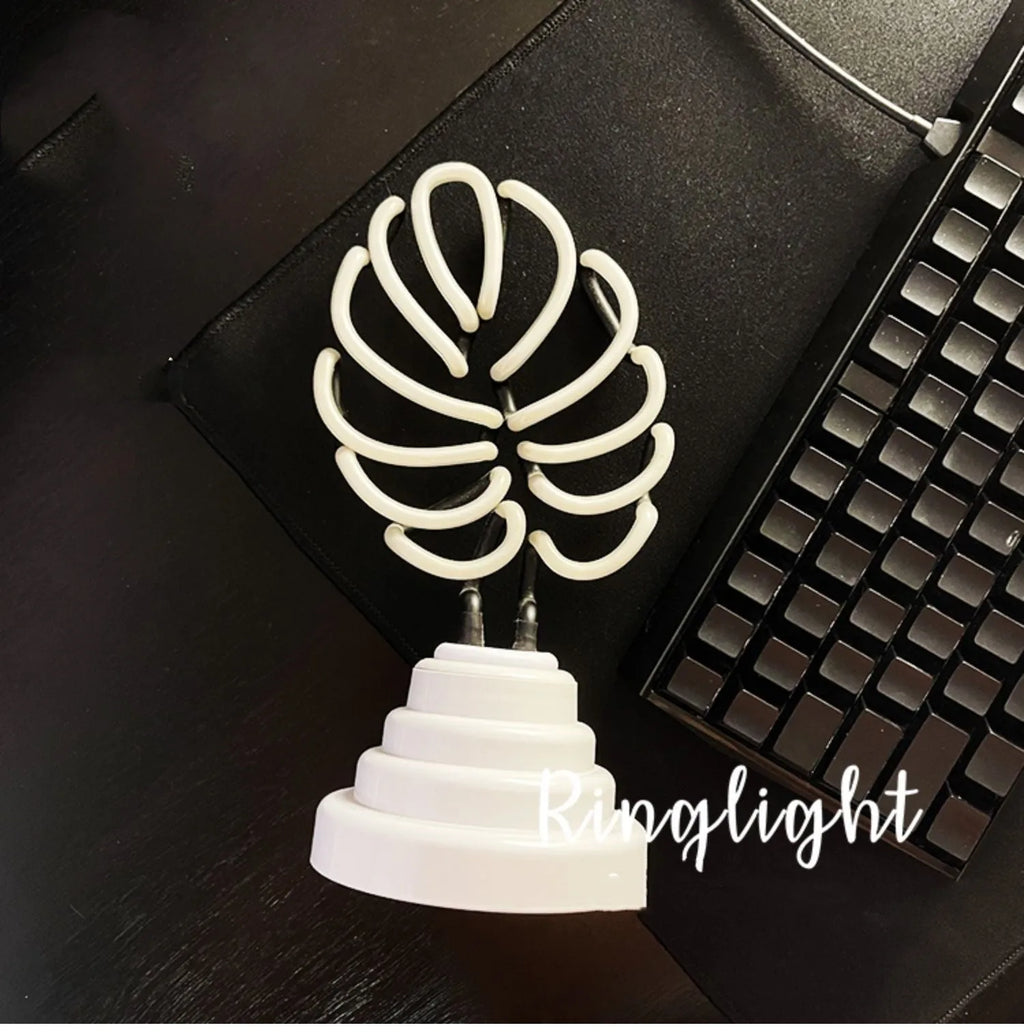 White bamboo-shaped desktop lamp with green light tube on a wooden desk.