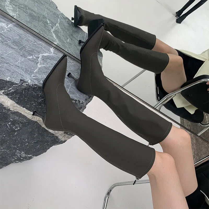 Black pointed toe below knee boots with stiletto heel and back zipper on woman's leg