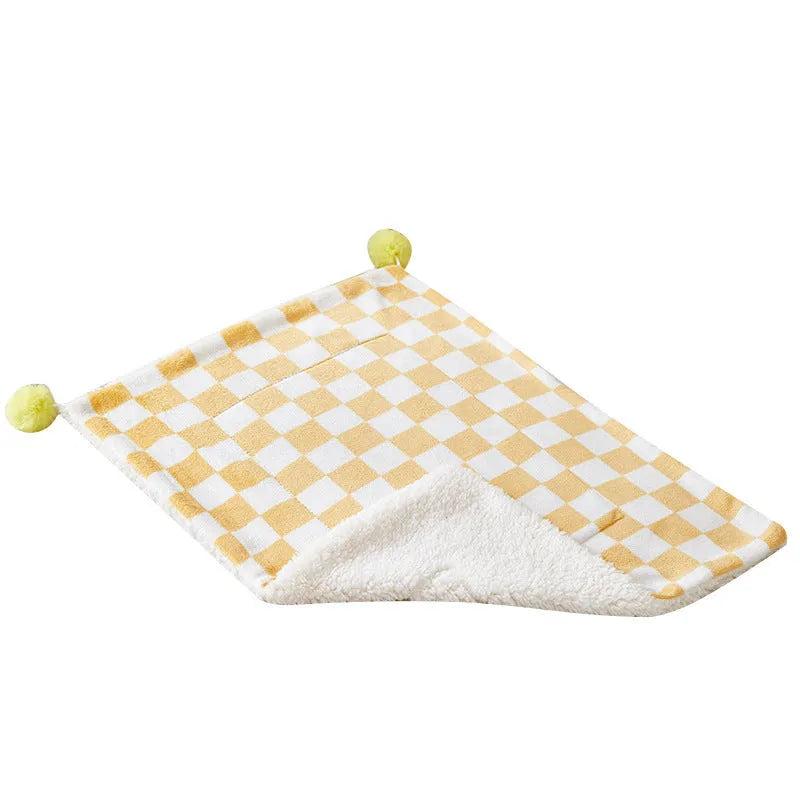 Green plaid pattern pet blanket with fur ball decoration on a sofa.