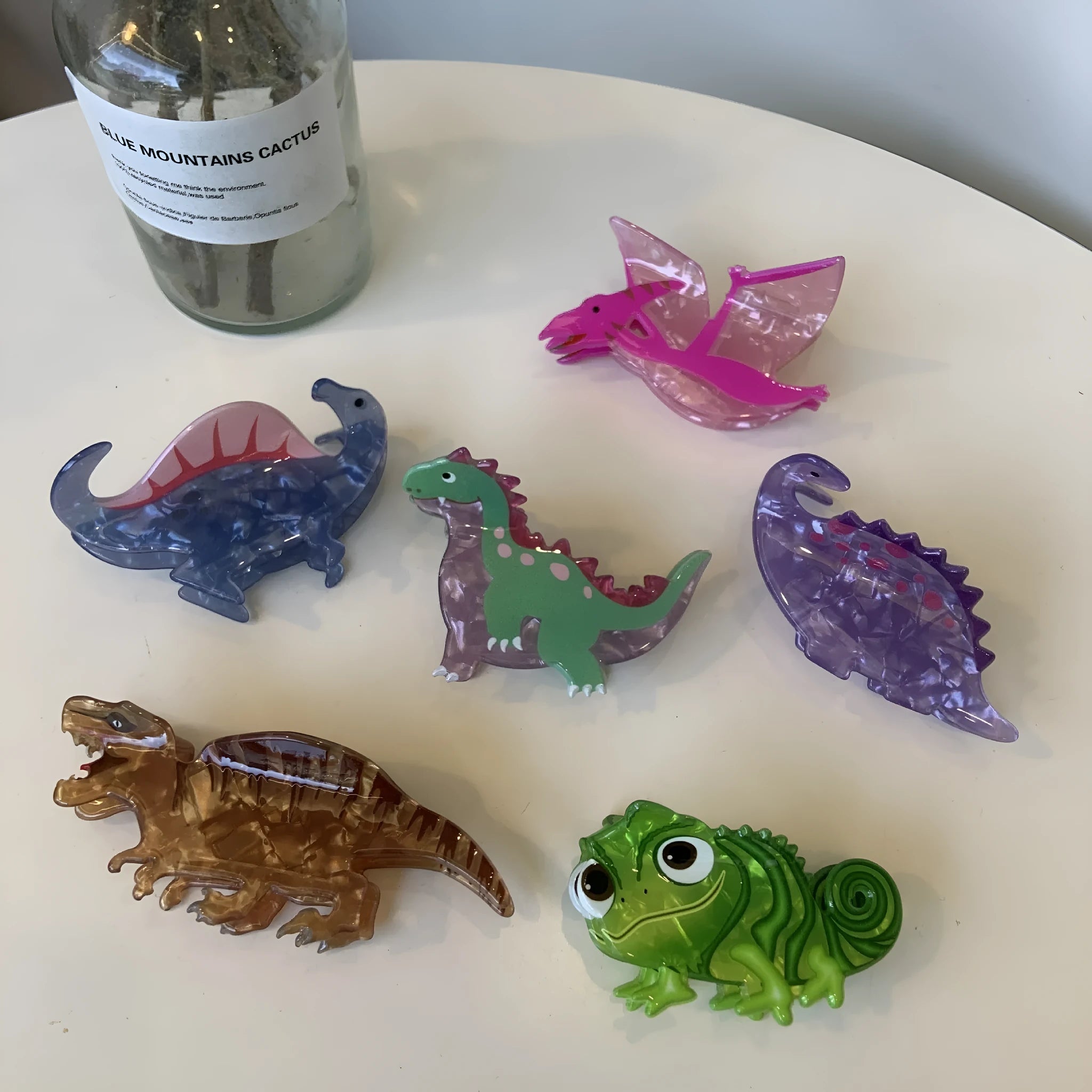 Acrylic dinosaur jaw grip hair clip showing six colour variations with prehistoric creature designs