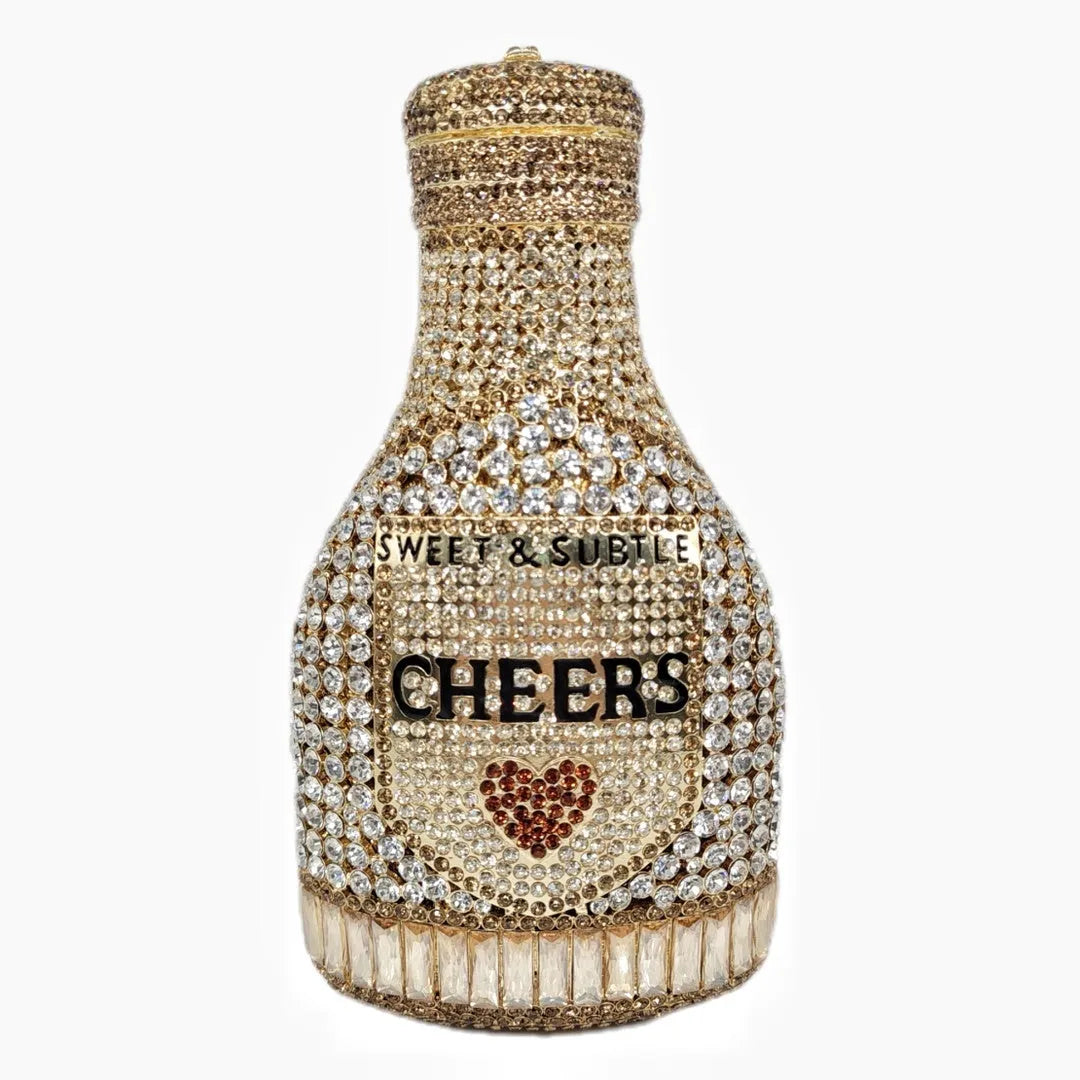 Gold hard-shell champagne bottle shaped evening clutch with rhinestones on a table.