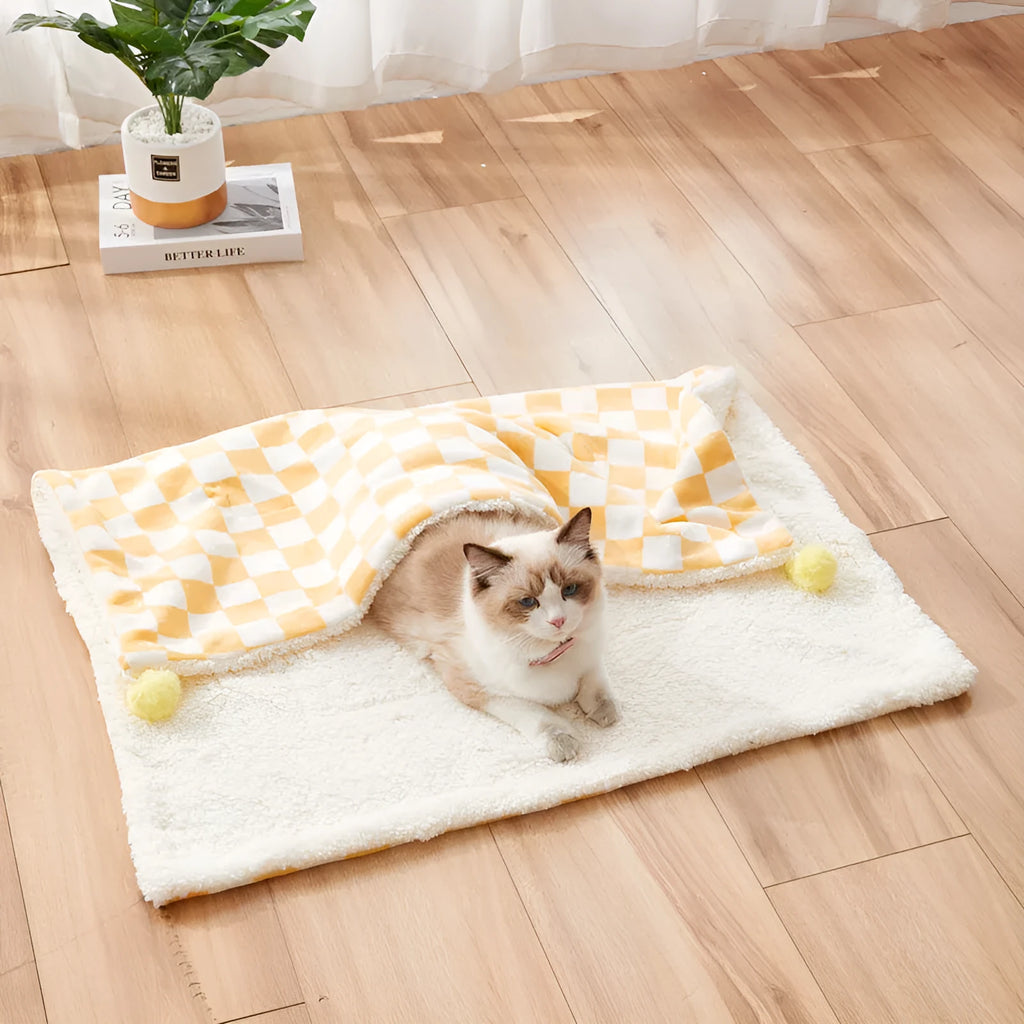 Green plaid pattern pet blanket with fur ball decoration on a sofa.