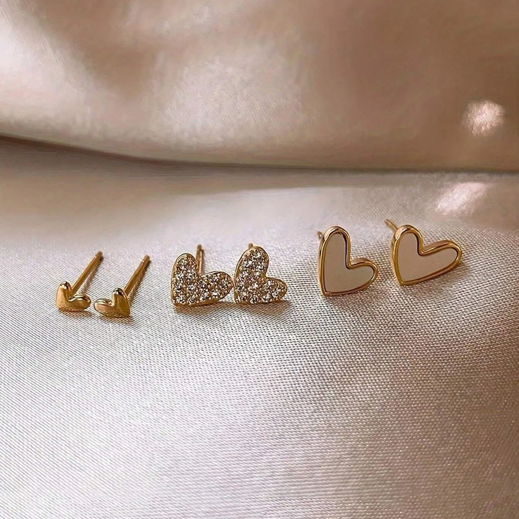Three pairs of heart-shaped electroplated alloy earrings in gold, black, black and white, and pink colour finishes