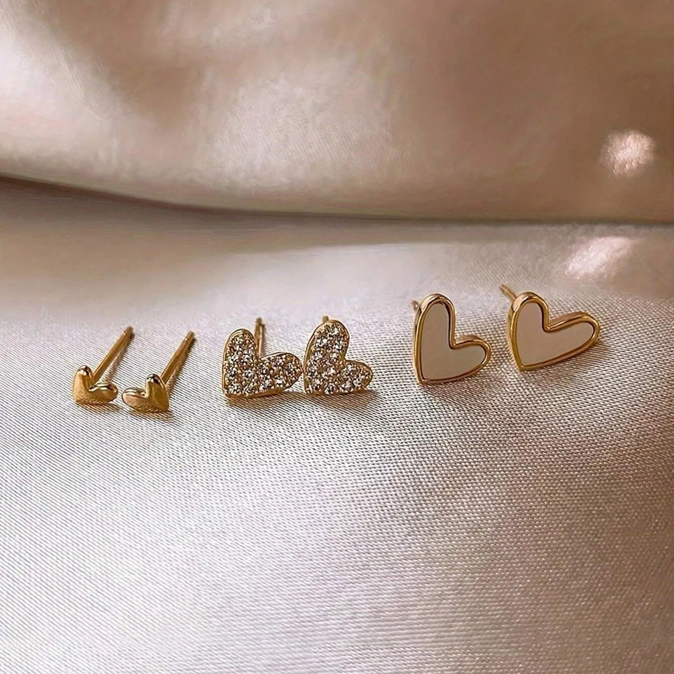 Three pairs of heart-shaped electroplated alloy earrings in gold, black, black and white, and pink colour finishes