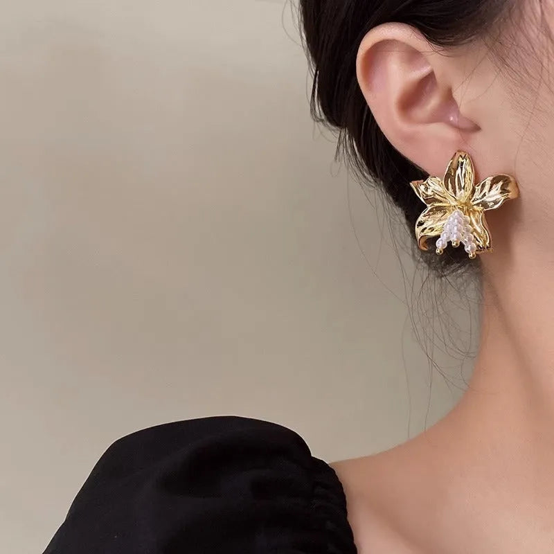 A pair of exaggerated gold metal flower earrings with pearls, showing niche style design.