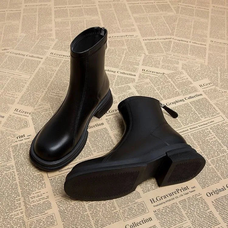 Women's black ankle boot with flat heel, round toe, and back zip on a plain background.