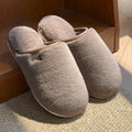 Solid colour PVC plush slippers with non-slip sole and car stitching detail on a wooden floor.