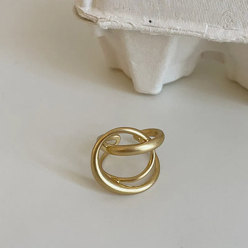 Matte metal open ring with three-dimensional interlaced geometric design in gold or silver finish.
