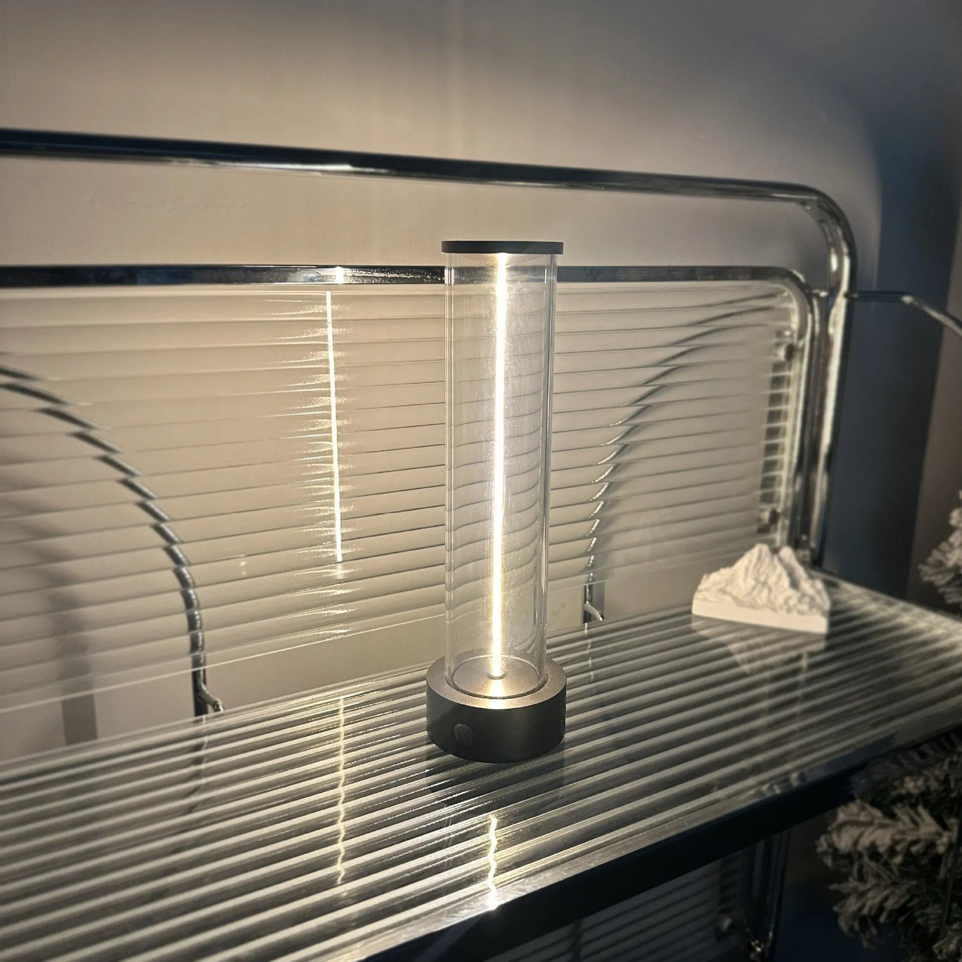 Glass cylindrical LED night light with magnetic base on a metal surface, showing USB charging port.