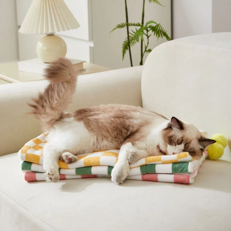 Green plaid pattern pet blanket with fur ball decoration on a sofa.