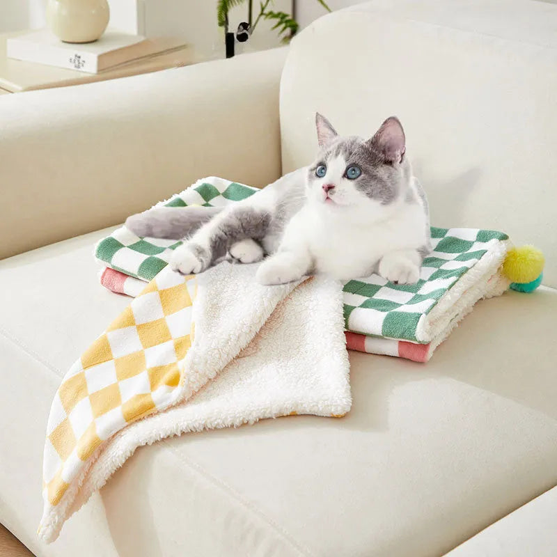 Green plaid pattern pet blanket with fur ball decoration on a sofa.