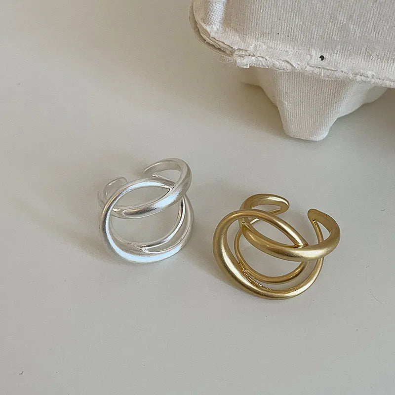 Matte metal open ring with three-dimensional interlaced geometric design in gold or silver finish.