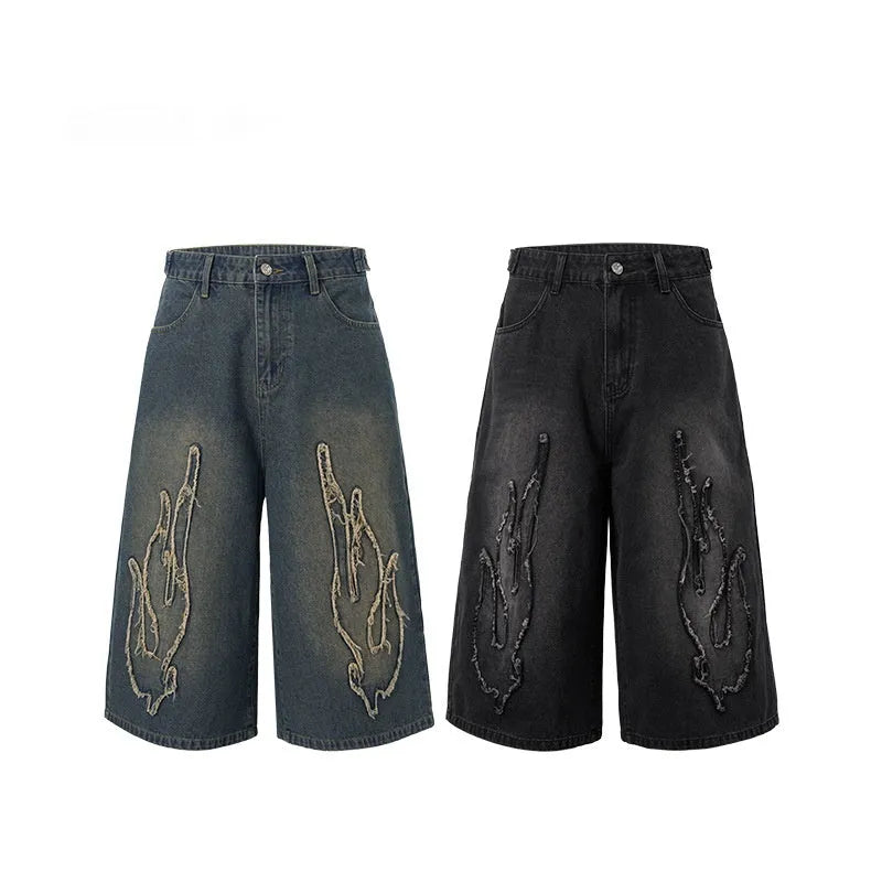 Men's black denim cropped shorts with red and yellow flame patch embroidery on the leg.