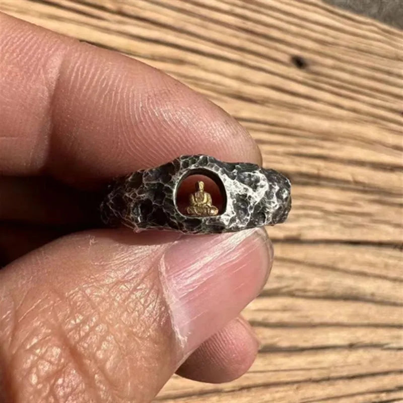 Close-up of a hand-forged copper ring with a rough rock texture and a detailed Buddha motif, shown on a finger.