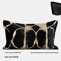 Black and gold abstract patterned flannel decorative pillow with removable cover on a grey sofa.