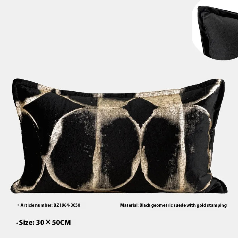 Black and gold abstract patterned flannel decorative pillow with removable cover on a grey sofa.
