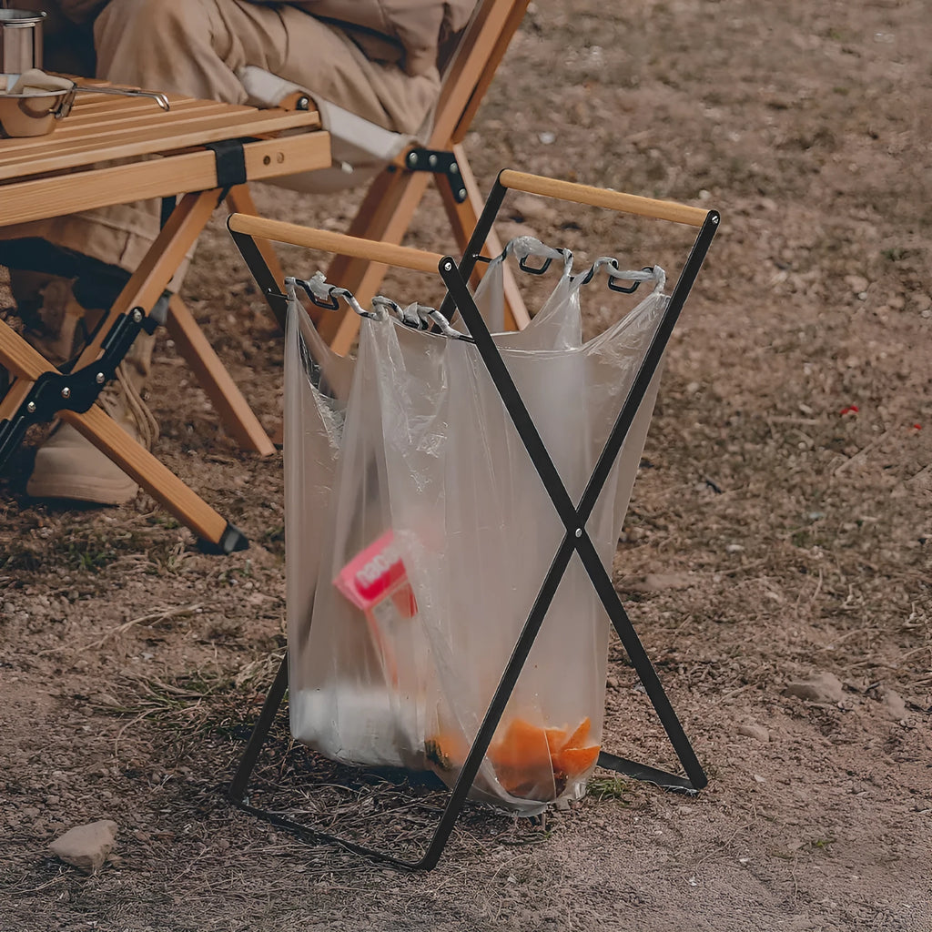 Black folding iron trash rack with wooden handles holding a bin bag outdoors