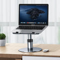 Silver adjustable aluminum laptop stand with non-slip pads on a desk next to a laptop.
