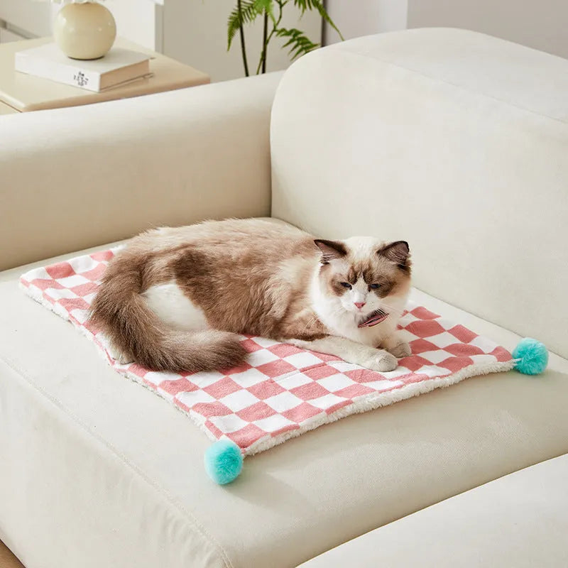 Green plaid pattern pet blanket with fur ball decoration on a sofa.