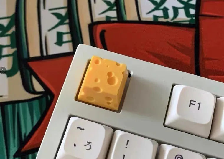Yellow resin mechanical keyboard keycap shaped like a cheese wedge with a cute character face.