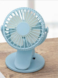 Small white USB rechargeable clip fan attached to a desk edge.
