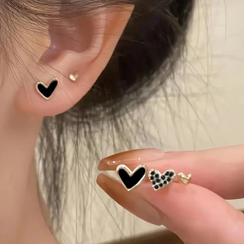 Three pairs of heart-shaped electroplated alloy earrings in gold, black, black and white, and pink colour finishes