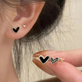 Three pairs of heart-shaped electroplated alloy earrings in gold, black, black and white, and pink colour finishes