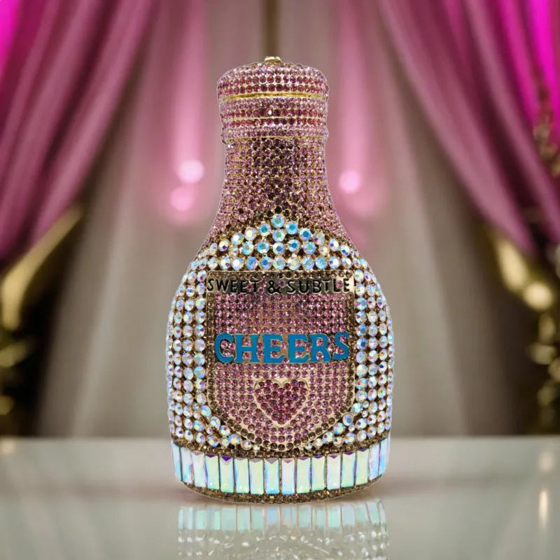 Gold hard-shell champagne bottle shaped evening clutch with rhinestones on a table.
