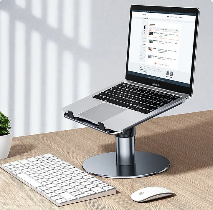 Silver adjustable aluminum laptop stand with non-slip pads on a desk next to a laptop.