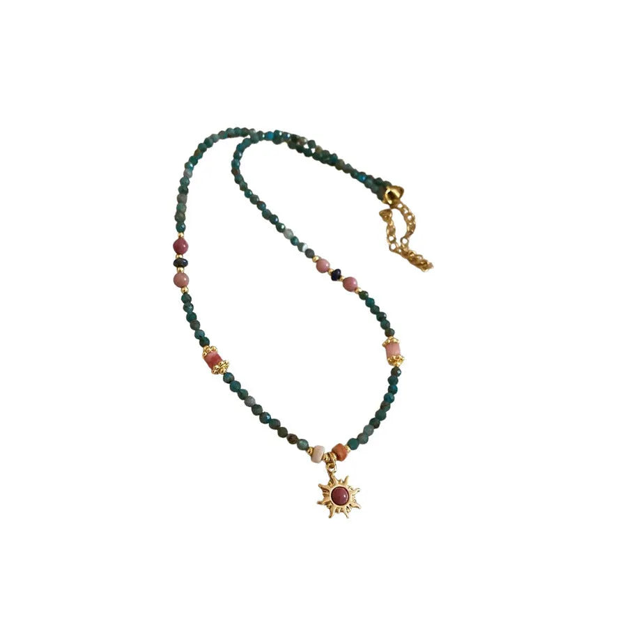 Close-up of a freshwater pearl and geometric stone sun necklace on an adjustable clavicle chain.