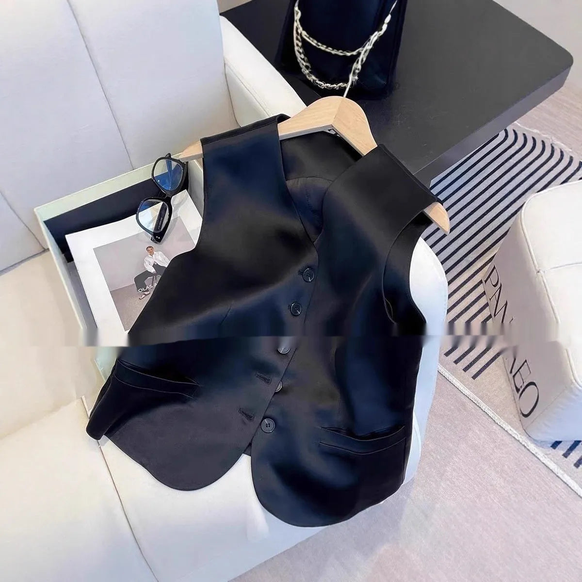 Black satin ladies' sleeveless vest with loose fit and splicing detail on a hanger.