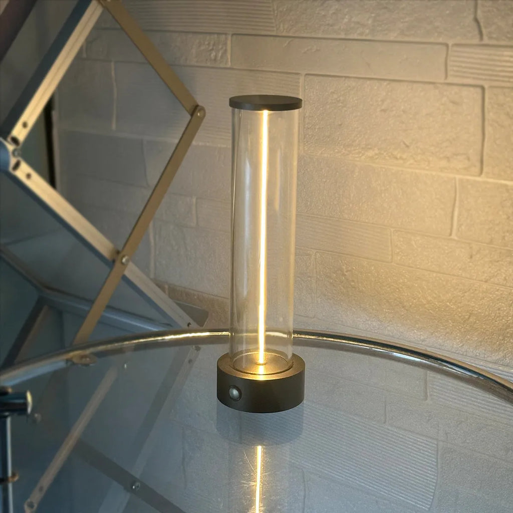 Glass cylindrical LED night light with magnetic base on a metal surface, showing USB charging port.