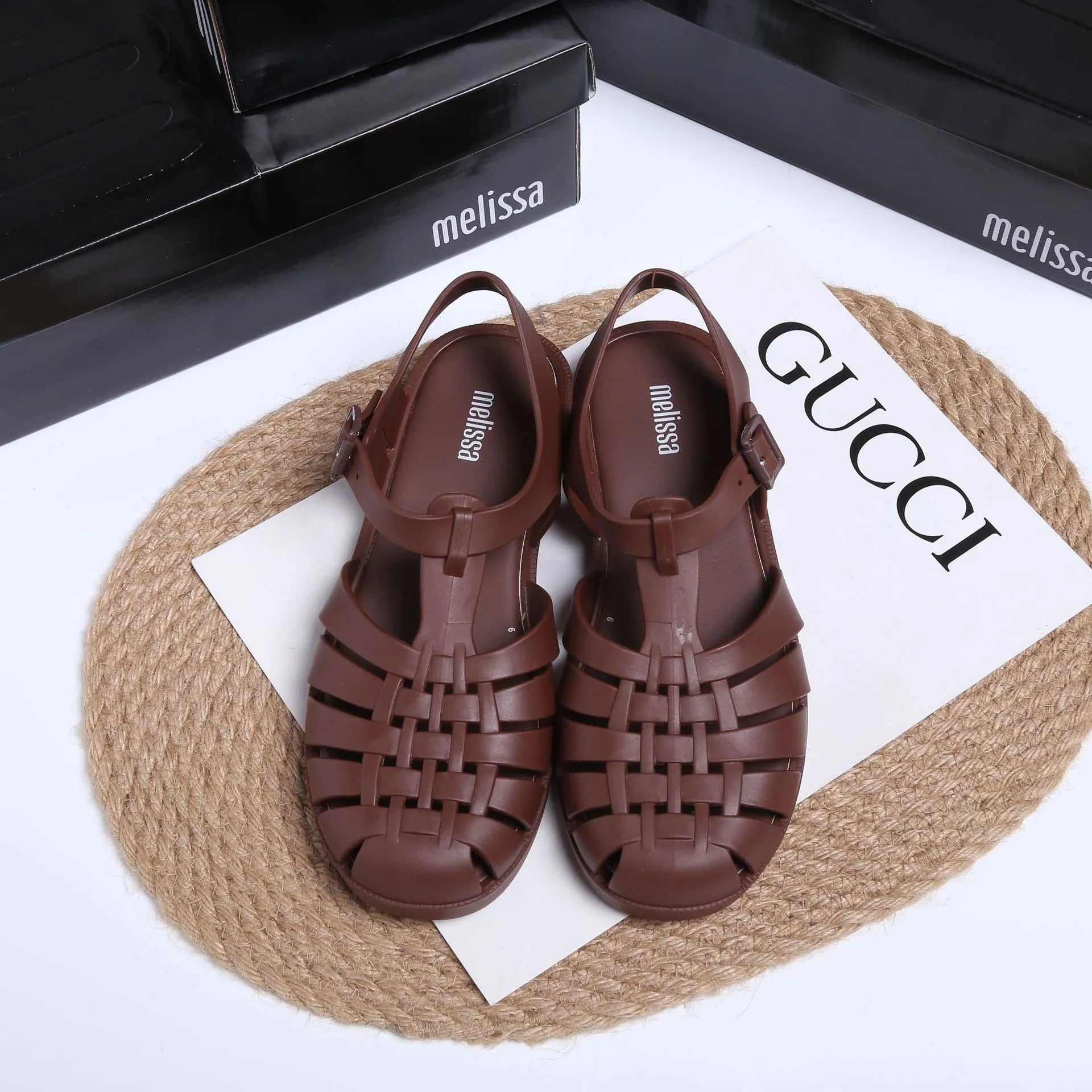 Matte black Roman style sandals with buckle fastening and PVC upper on wooden surface