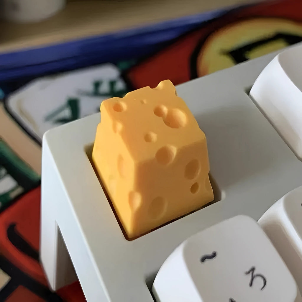 Yellow resin mechanical keyboard keycap shaped like a cheese wedge with a cute character face.