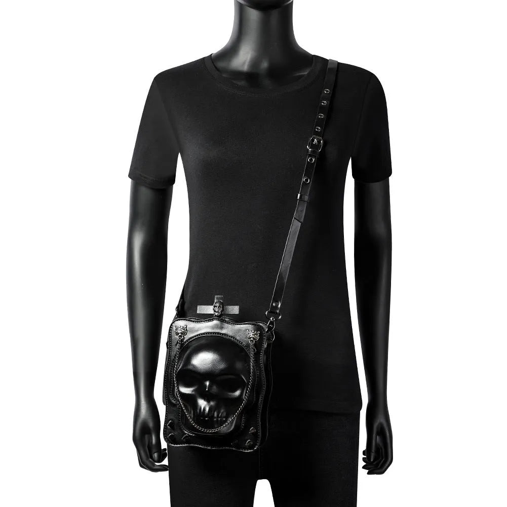 Black mini square crossbody bag with embossed skull design, decorative stitching, rivets, and chain details.