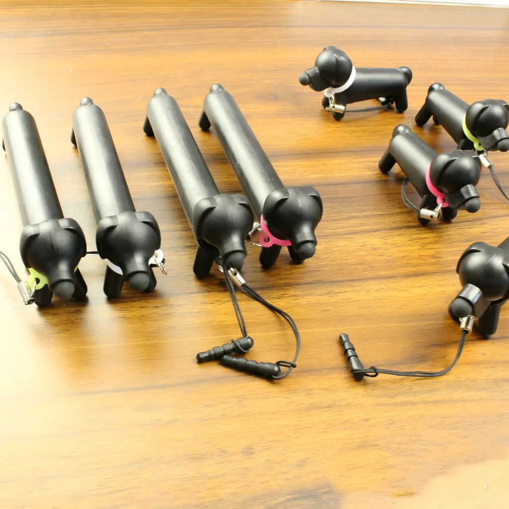 Black dog-shaped touch screen stylus with conductive body shown next to smartphone demonstrating phone holder function