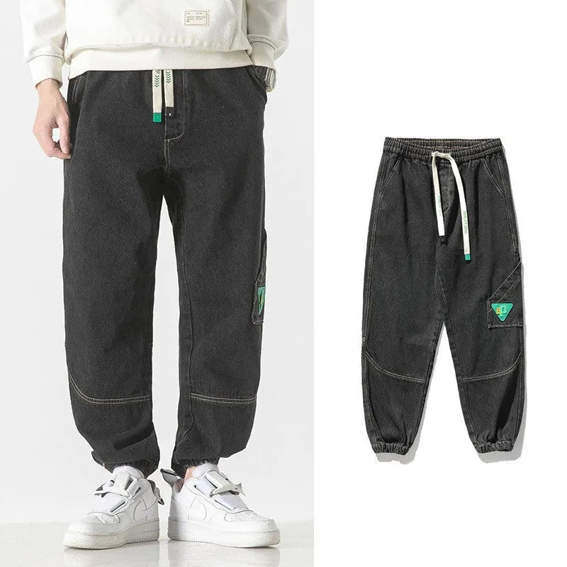 Men's black loose-fit tapered cotton trousers on a hanger, showing the mid-waist and tapered leg design.