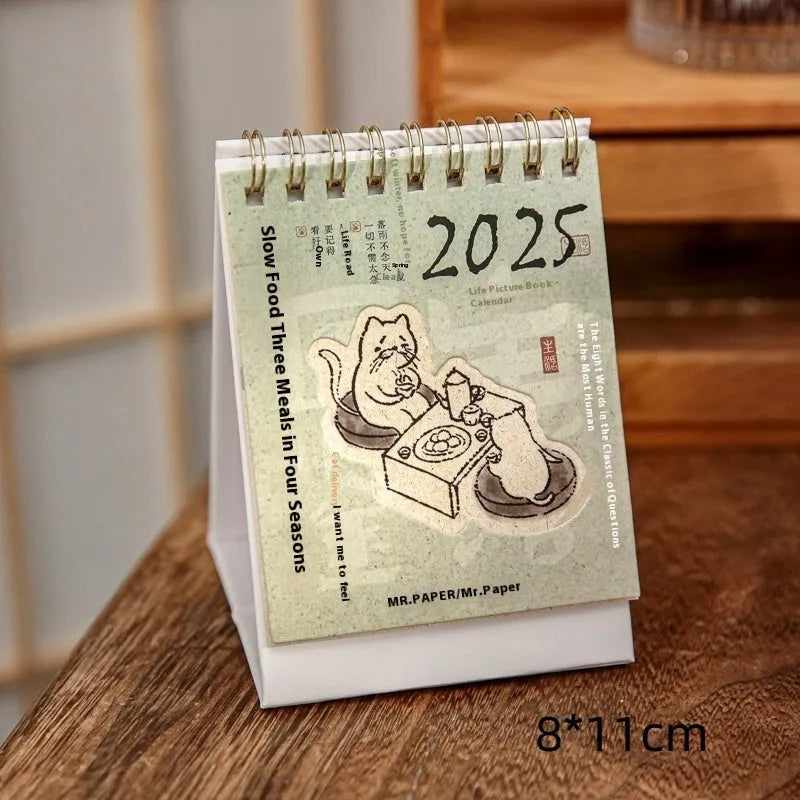 Mini A6 paper desk calendar for 2025 open to a monthly page with coffee-themed design.