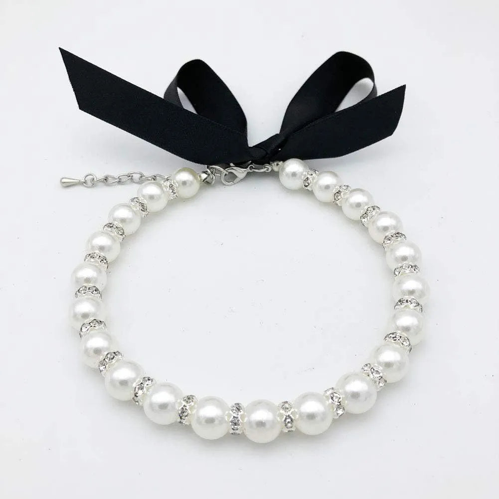 Small dog wearing a blue adjustable pearl and rhinestone necklace with a ribbon bow.