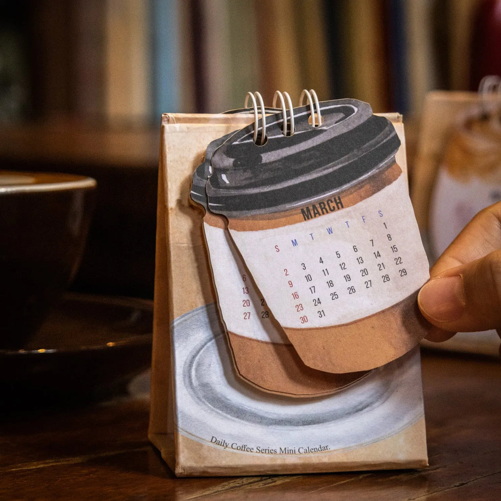 Mini A6 paper desk calendar for 2025 open to a monthly page with coffee-themed design.