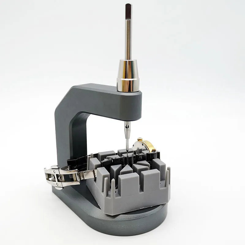 Silver tool steel multi-purpose press strap removal tool for watches and electronics on a workshop surface.