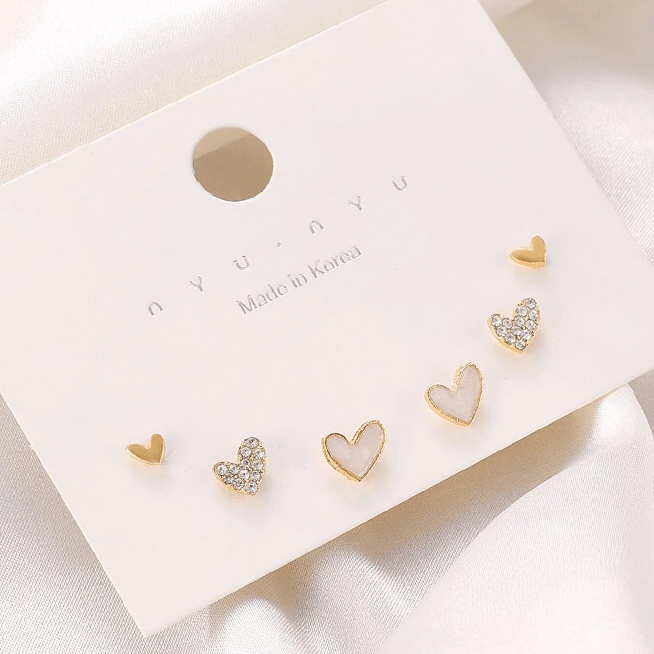 Three pairs of heart-shaped electroplated alloy earrings in gold, black, black and white, and pink colour finishes