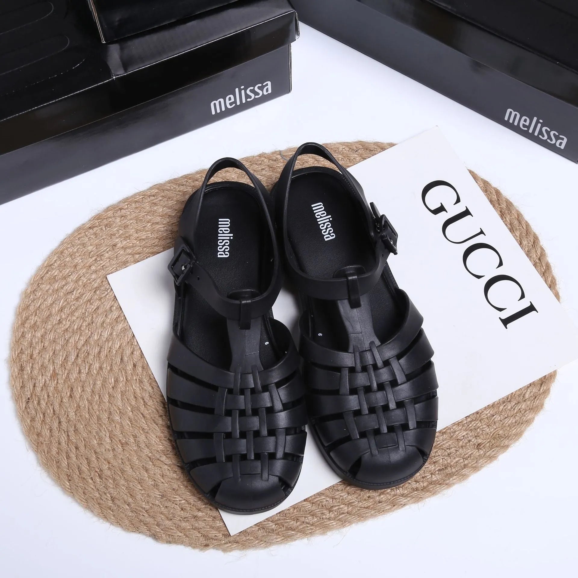 Matte black Roman style sandals with buckle fastening and PVC upper on wooden surface