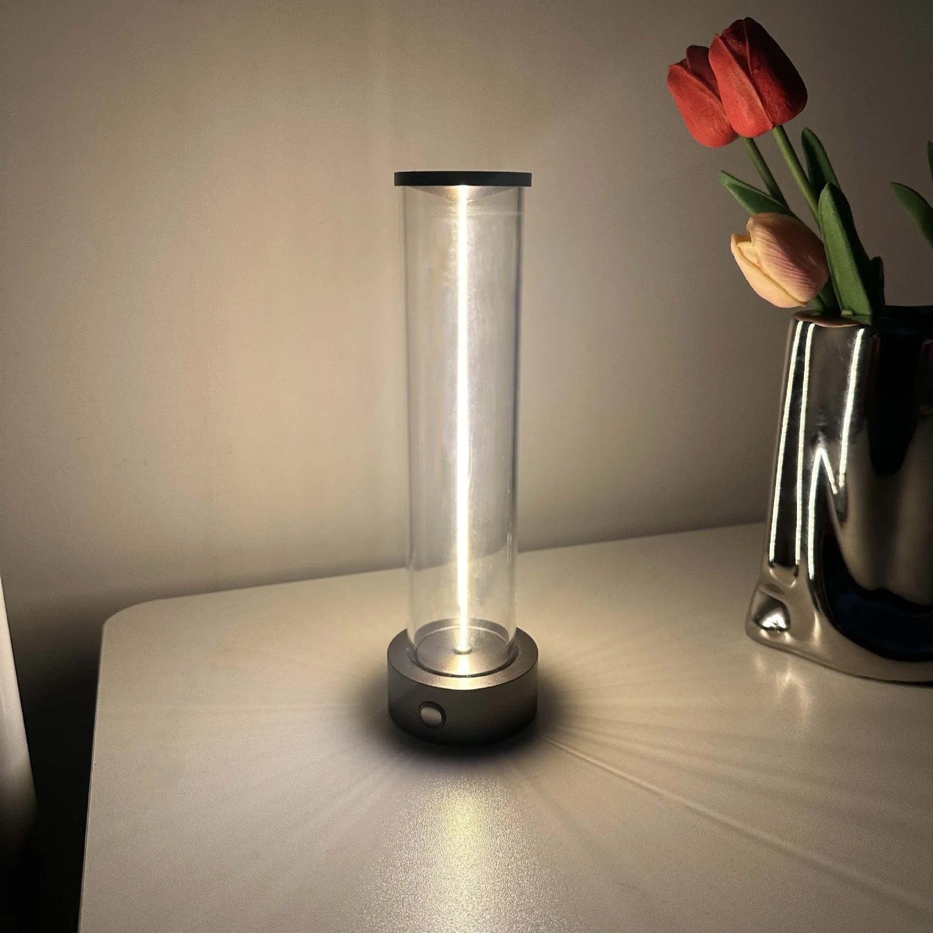 Glass cylindrical LED night light with magnetic base on a metal surface, showing USB charging port.