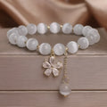 White cat's eye stone flower bracelet with silver-tone details and a hanging tassel charm.