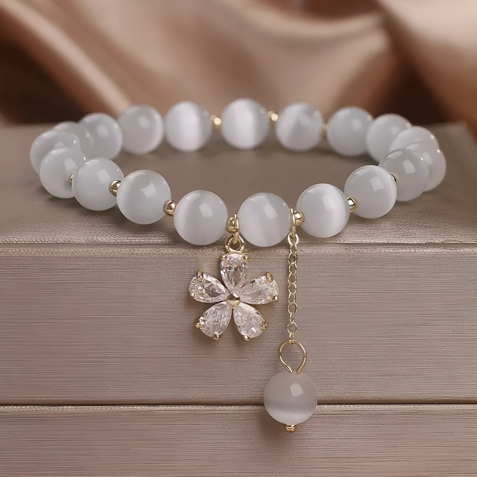 White cat's eye stone flower bracelet with silver-tone details and a hanging tassel charm.
