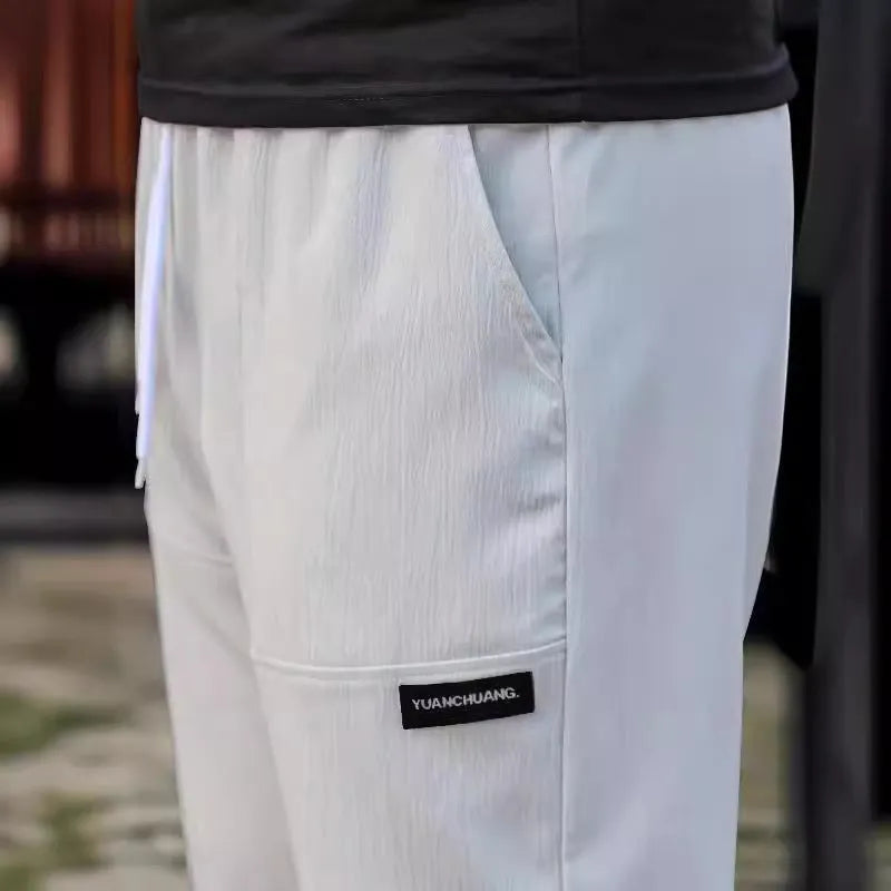 Men's polyester trousers in light grey, shown laid flat, suitable for spring and autumn wear.