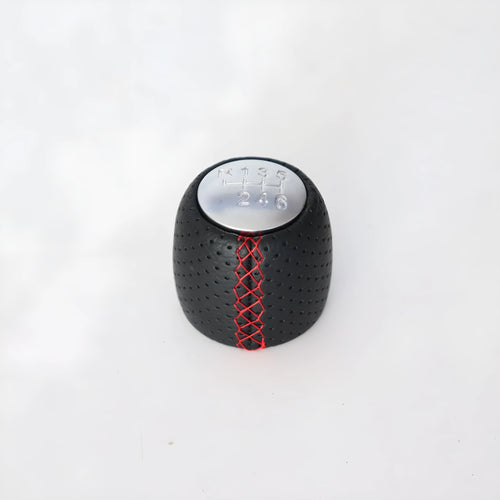 Sewn wrapped black perforated leather gear shift handball for Alpha vehicles on a silver cover.