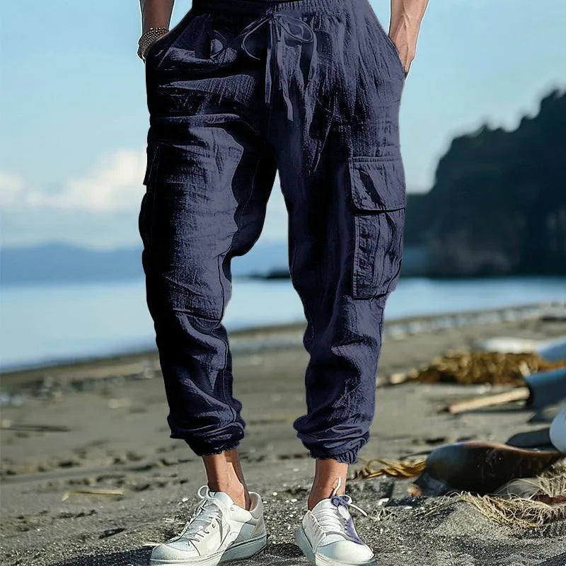 Man wearing loose, ankle-tied linen trousers in a solid colour with visible pockets.