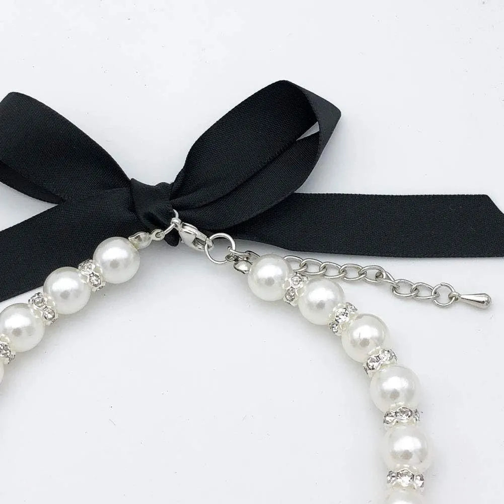 Small dog wearing a blue adjustable pearl and rhinestone necklace with a ribbon bow.